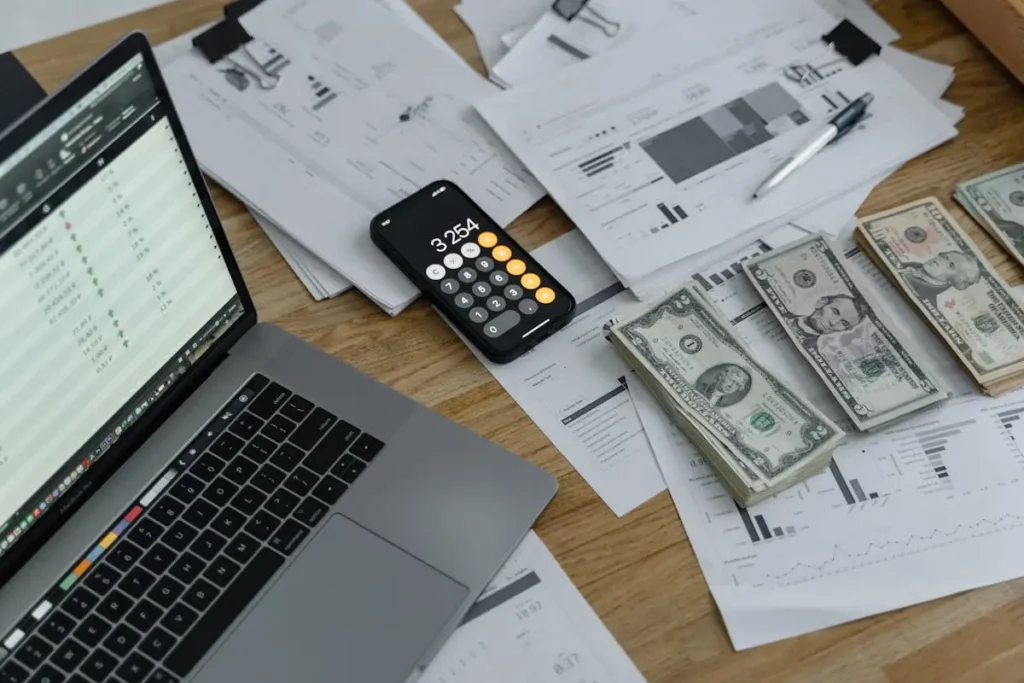A budgeting setup with a laptop, financial documents, a smartphone calculator, and cash stacks, illustrating how to budget effectively and manage expenses.
