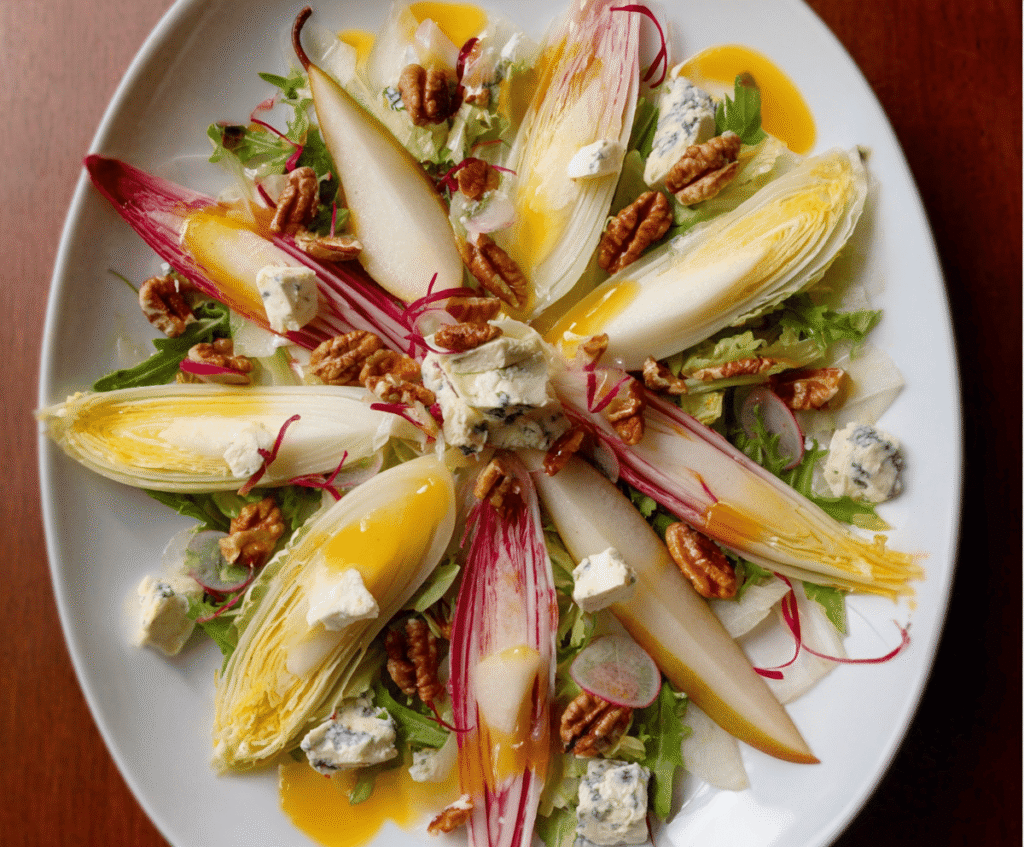 Fresh endive and ripe pear salad with walnuts and blue cheese crumbles on a white plate.