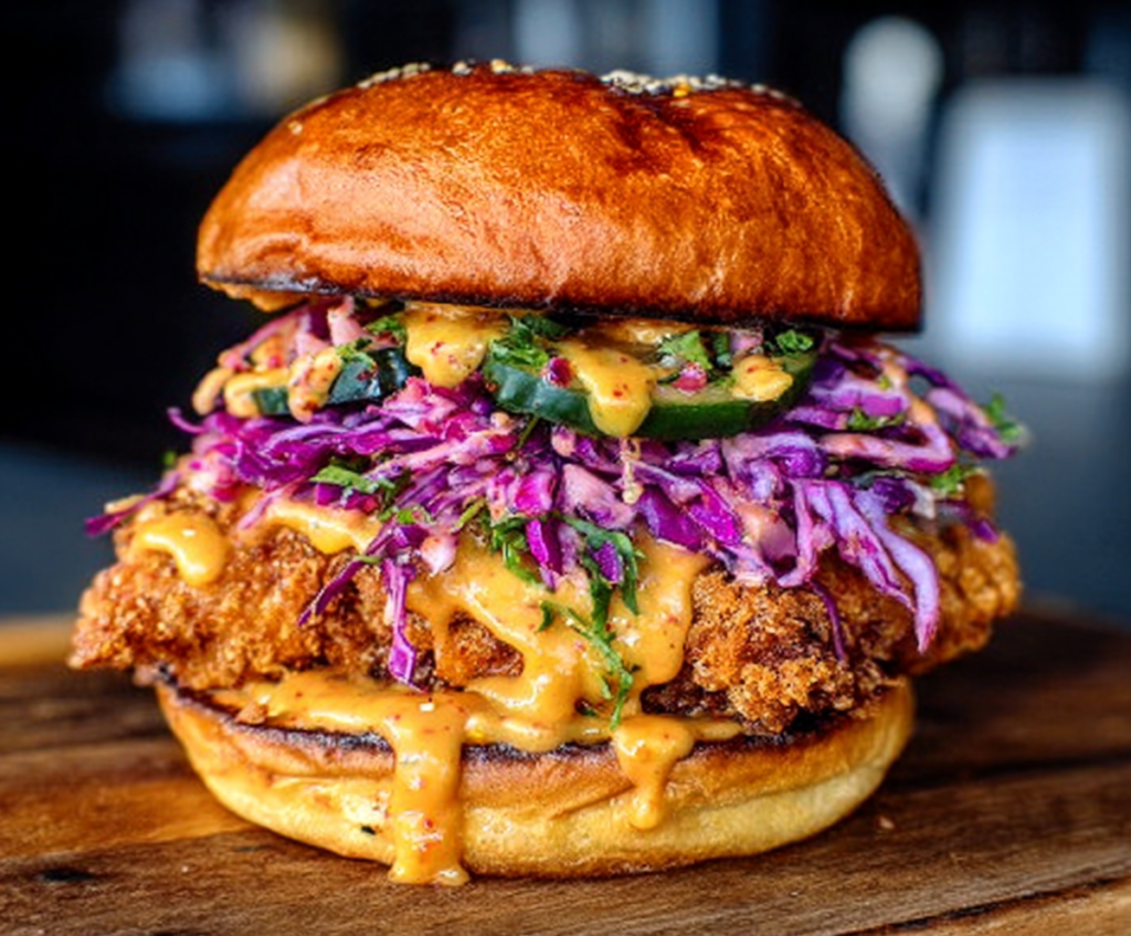 Crispy Bang Bang Chicken Sandwich topped with spicy sauce and fresh greens on a plate.