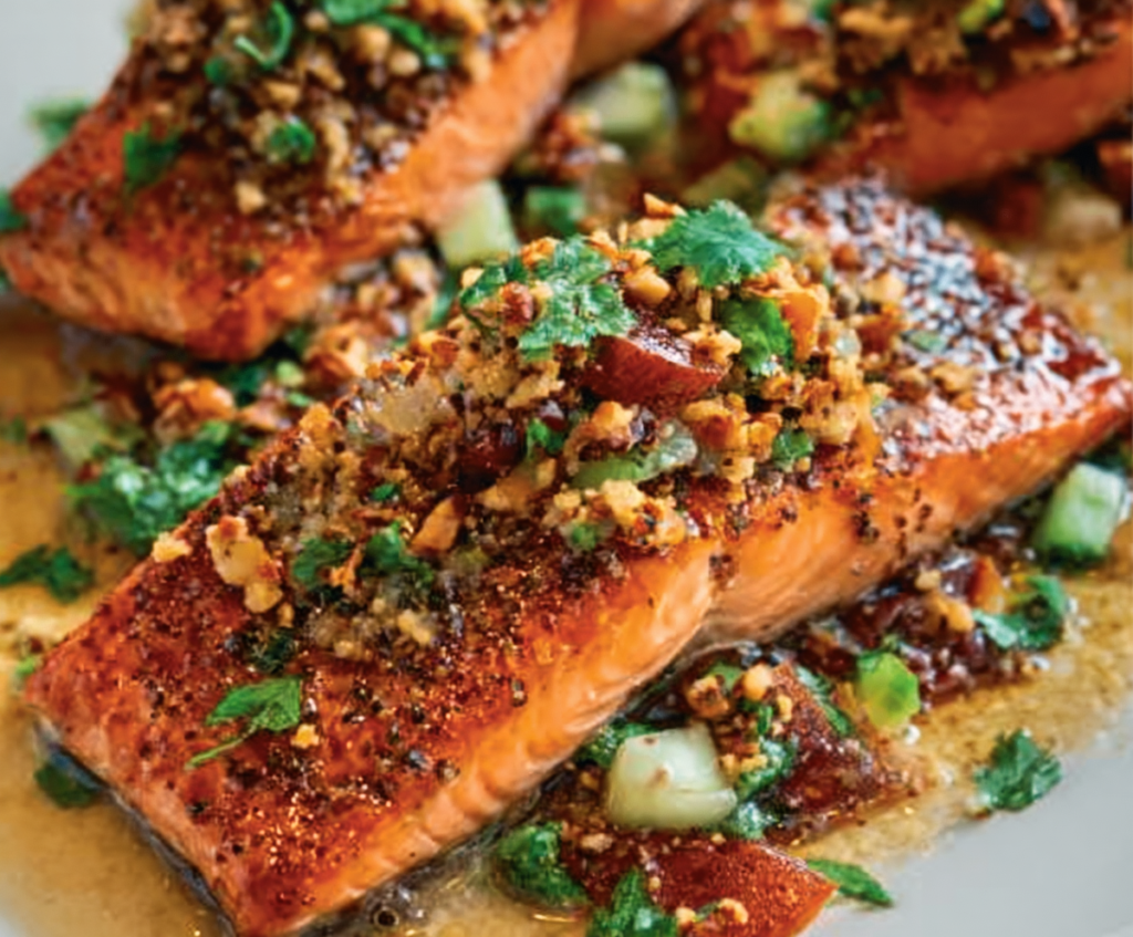 Delicious salmon fillet topped with vibrant sizzled nut salsa, garnished with fresh herbs.